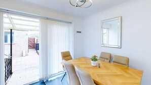 A modern dining room with a wooden table, four chairs, a potted plant, and a ceiling light fixture. - Ranworth House - Holiday Home in Bedford, Sleeps 5 (Bedford)