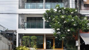 A multi-story building named 'Chiang Mai Mansion II' with a balcony, a staircase leading to the entrance, and potted plants in front.