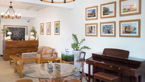 A room with a piano, a glass table, wooden furniture, a reception desk, and framed pictures on the wall.