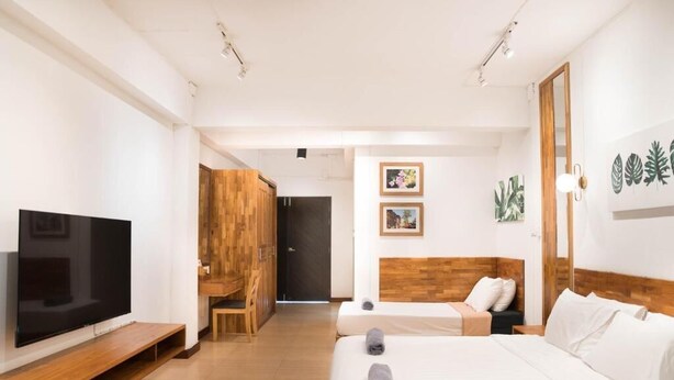 A hotel room with a bed, a TV, a wooden wardrobe, and a door leading to another room.