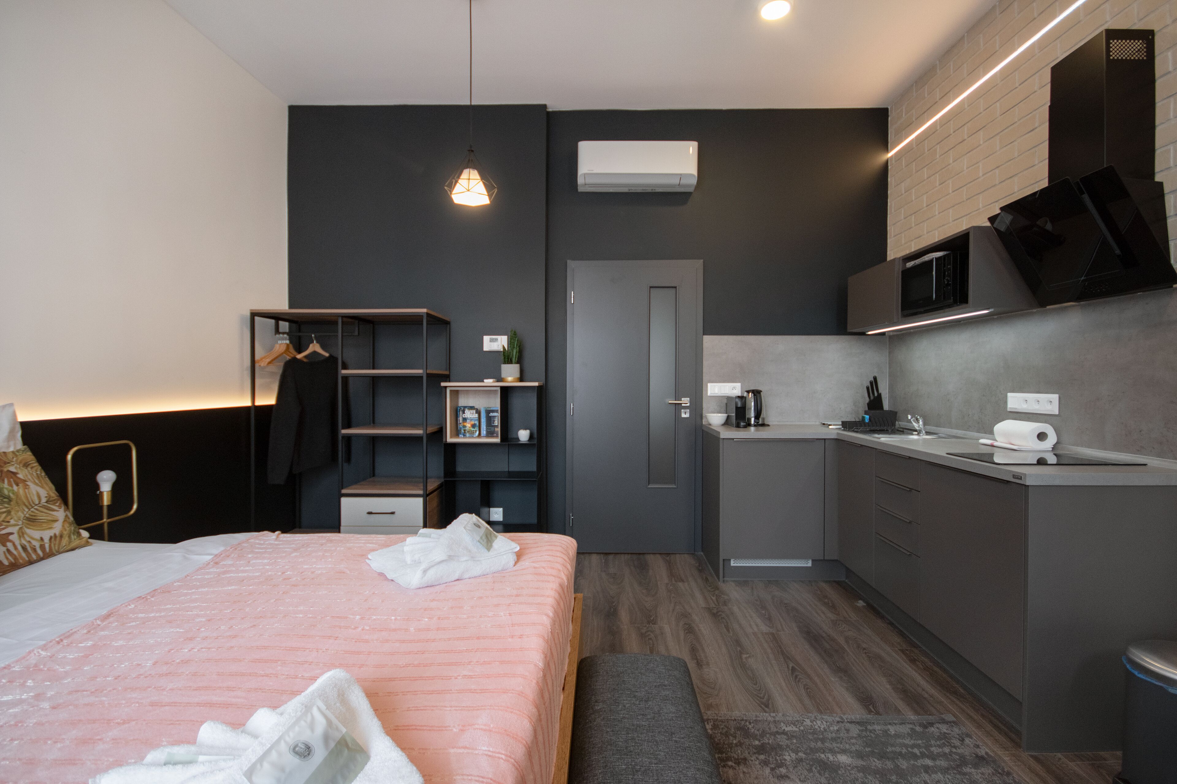 A modern hotel room with a bed, bedside table, and a small kitchenette.