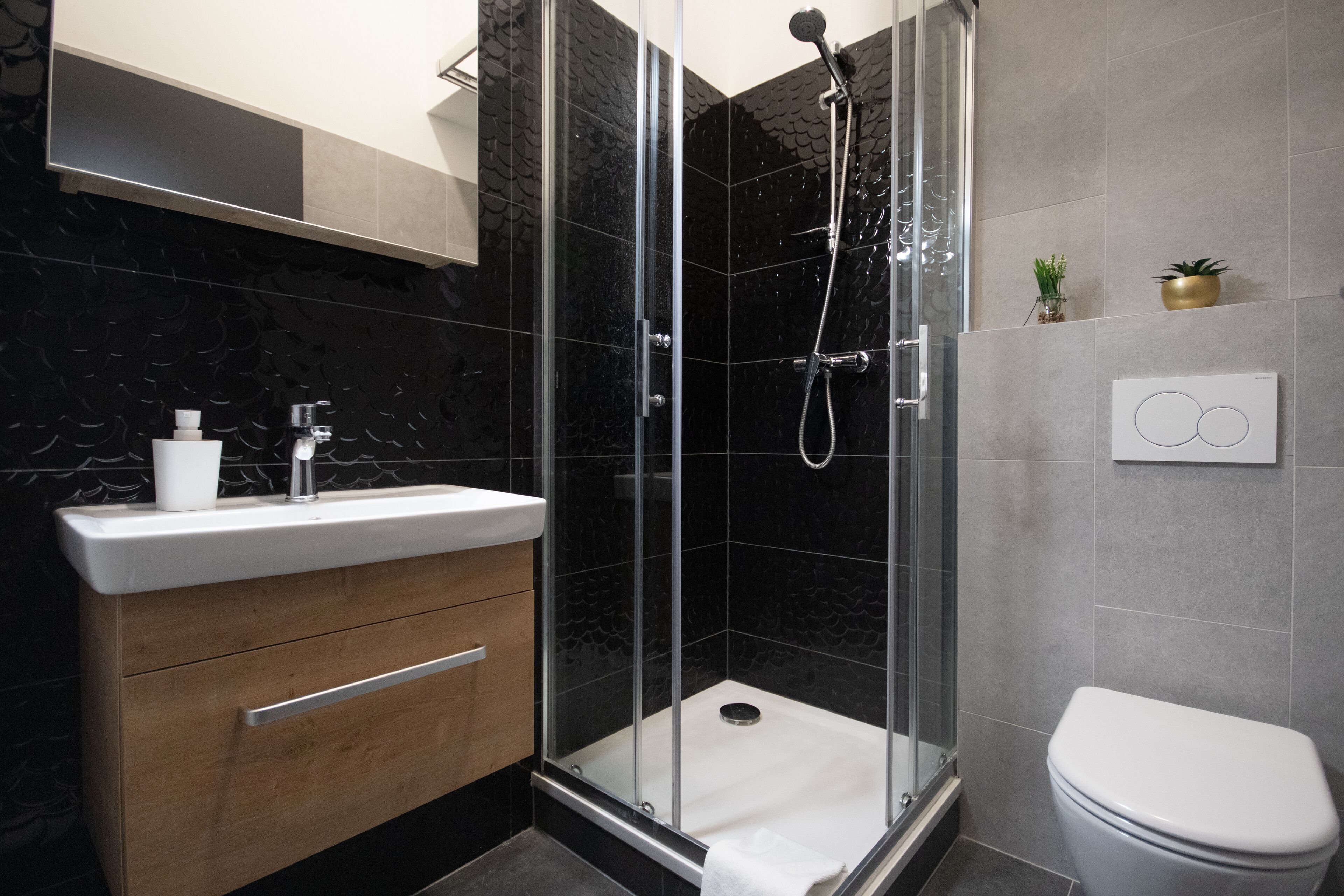 A modern bathroom with a glass-enclosed shower, a white sink with a wooden cabinet, and a toilet.