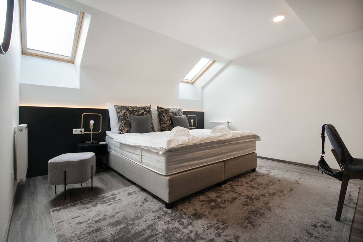 A modern bedroom with a large bed, a skylight, a nightstand, and a chair.