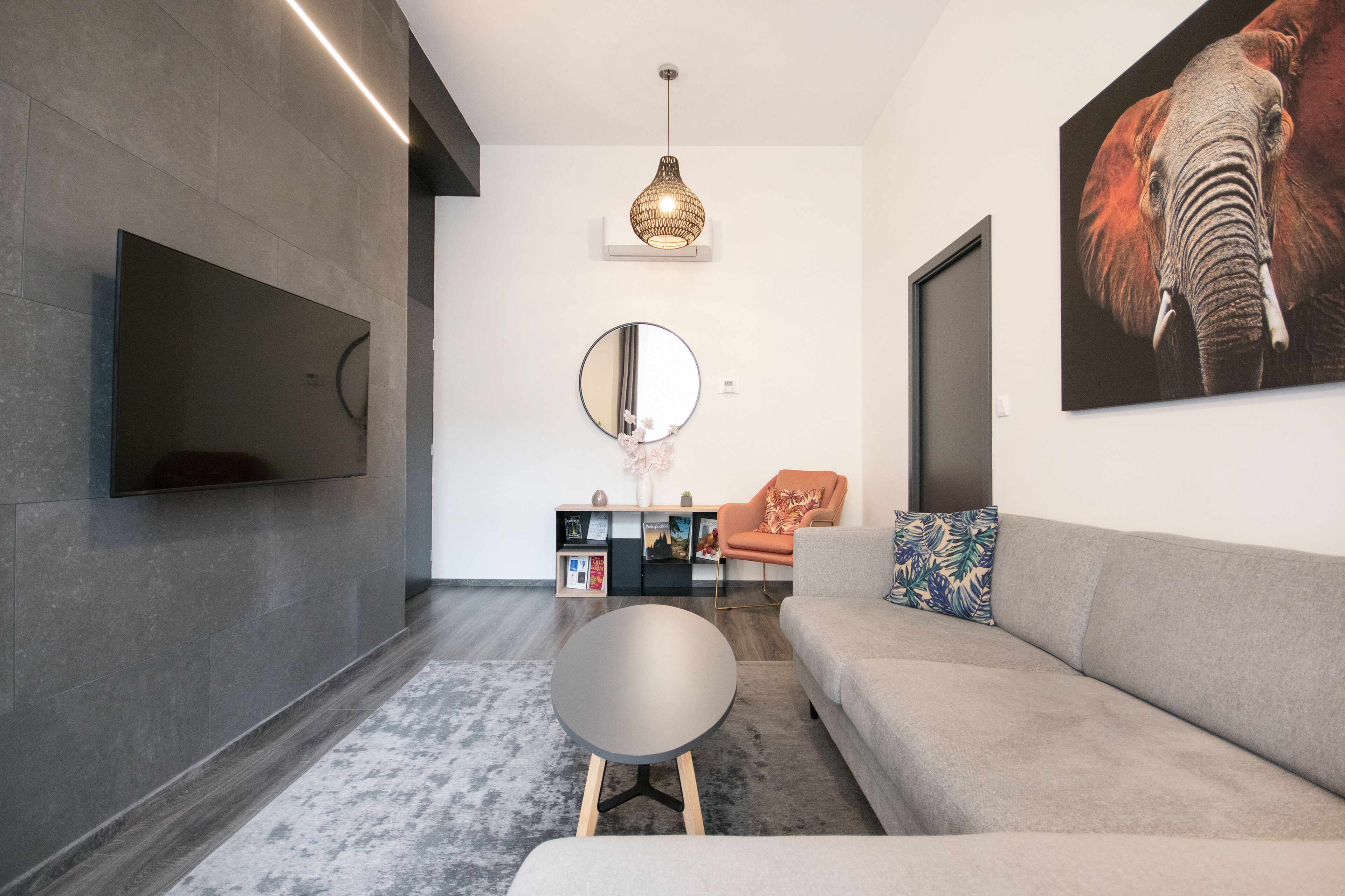 Una sala de estar moderna con un televisor de pantalla plana, un espejo redondo, un sofá y un cuadro decorativo de un elefante.