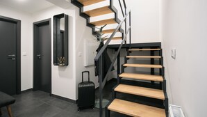 A modern staircase with wooden steps and metal railings, a black suitcase, and a mirror on the wall. - CORU House (Prague)