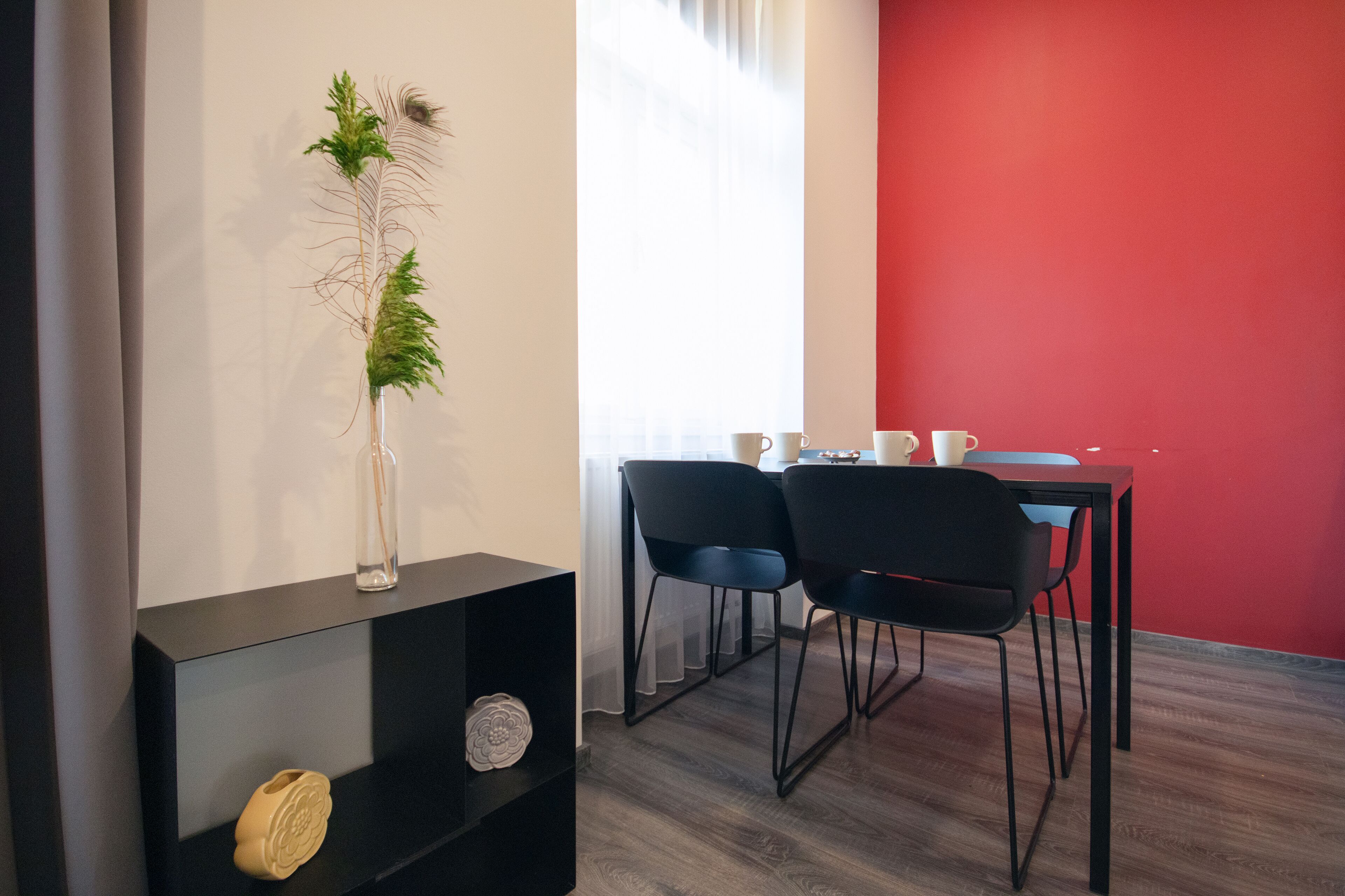 A modern dining area with a red accent wall, a black table, and two black chairs.