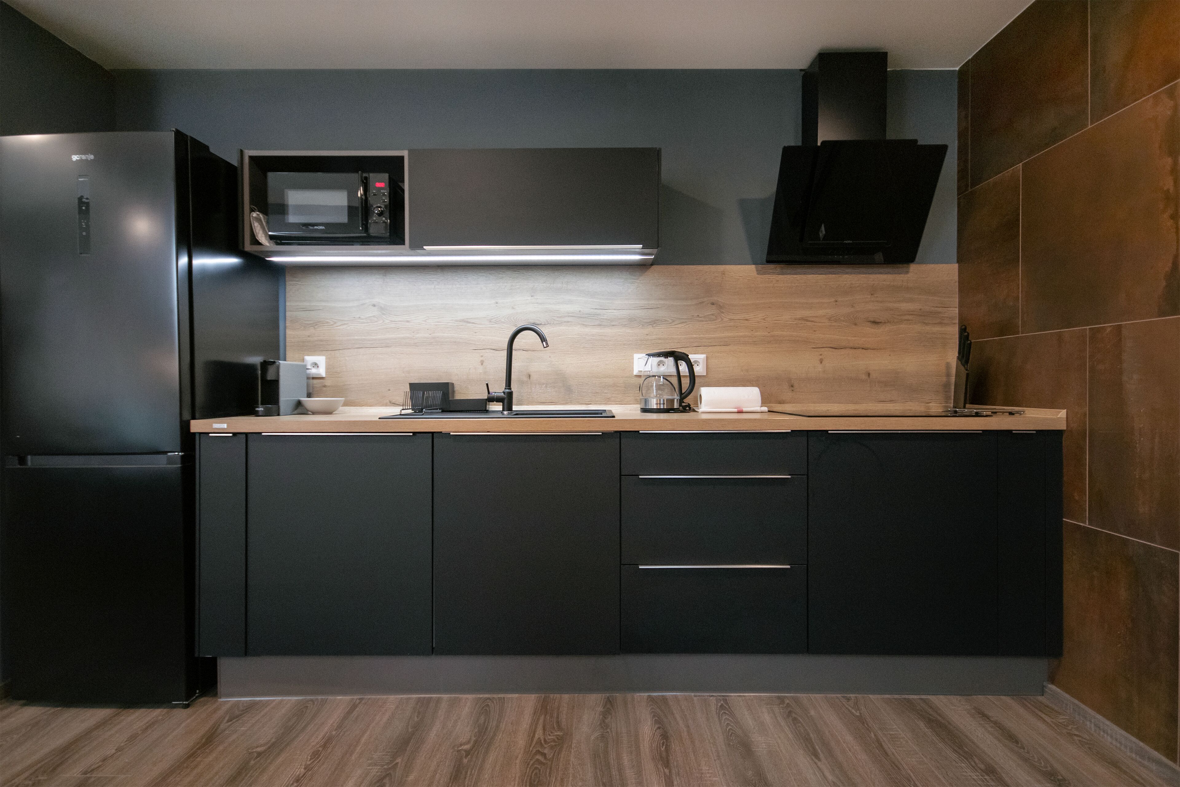 Una cocina moderna con un refrigerador negro, un microondas, un lavamanos y armarios de madera.