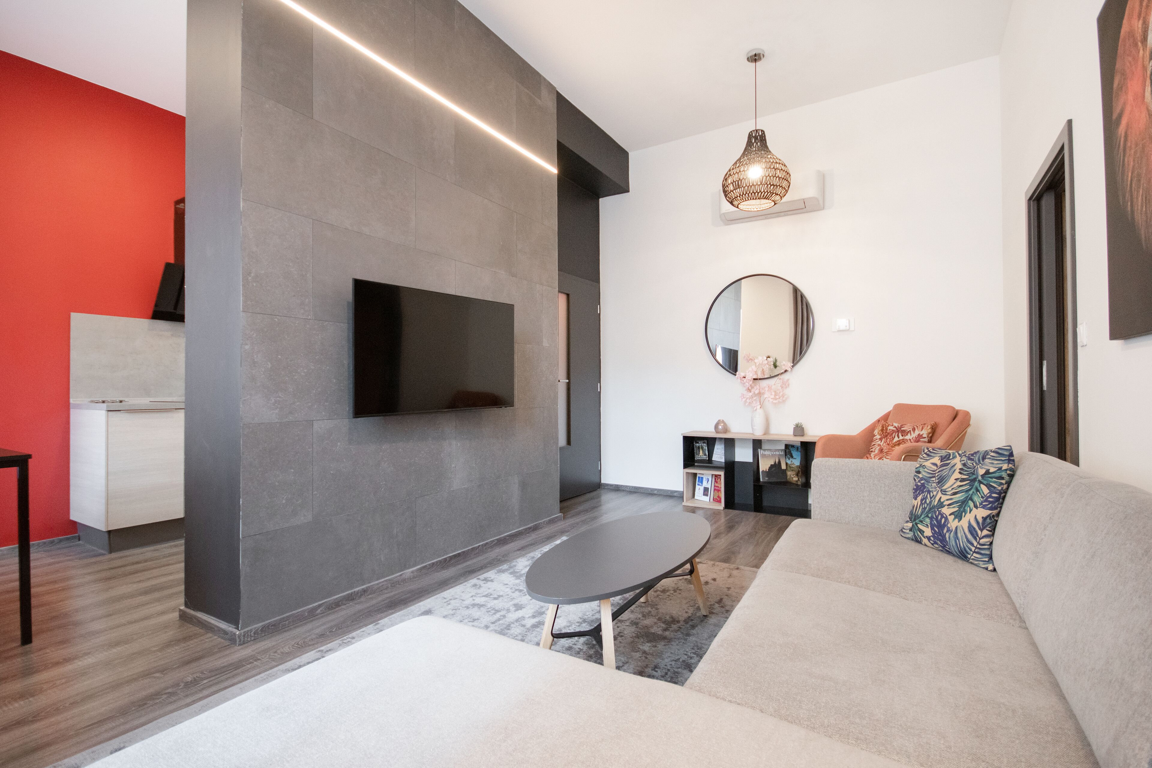 A modern living room with a grey sofa, a small round table, and a flat-screen TV mounted on the wall.