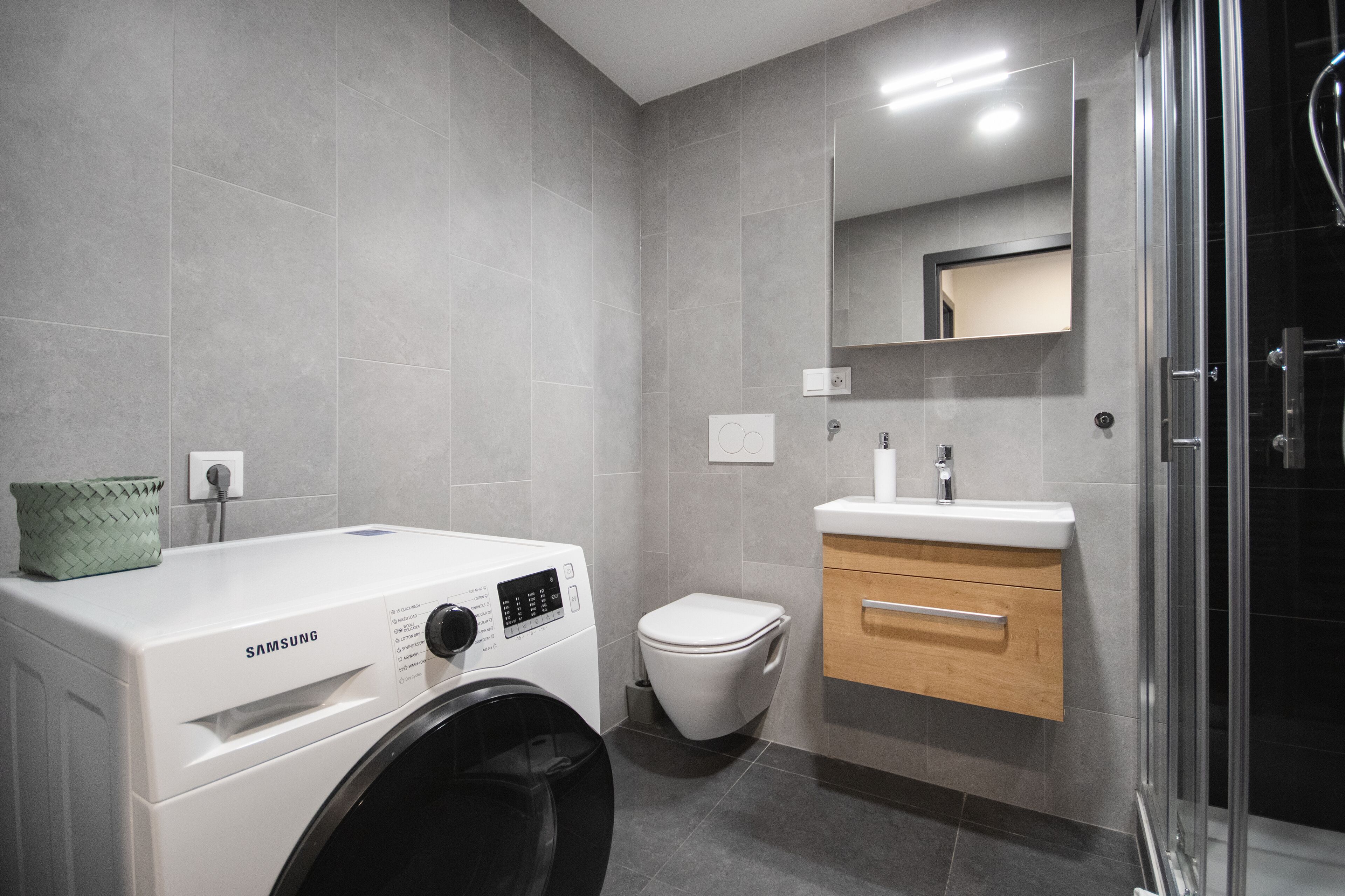 Un baño moderno con lavadora, inodoro, lavabo y cabina de ducha de vidrio.