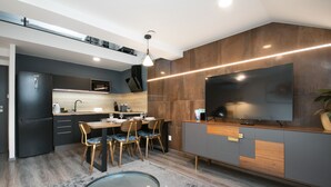 A modern kitchen with a dining area, featuring a large flat-screen TV, wooden cabinets, and a built-in microwave. - CORU House (Prague)