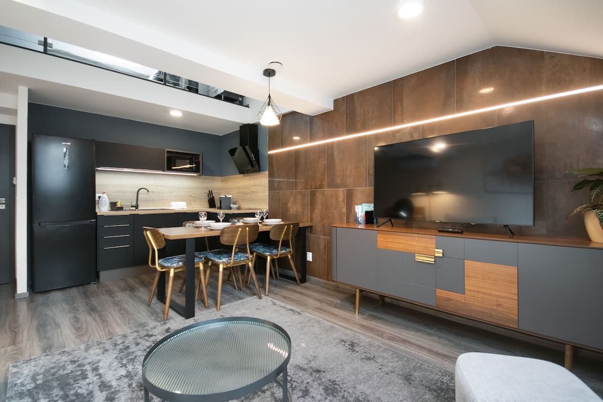 A modern kitchen with a dining area, featuring a large flat-screen TV, wooden cabinets, and a built-in microwave.