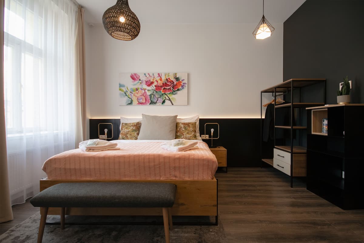 A modern bedroom with a large bed, bedside tables, a bench, and a wall-mounted shelf.
