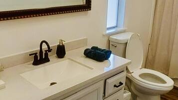 A bathroom with a white sink, black faucet, and a toilet. There is a window above the toilet and a mirror above the sink.