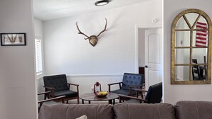 A living room with a brown leather sofa, a round coffee table, and a mounted deer head on the wall. There are two chairs and a small table with a lantern and a bowl. - Cozy Lake House Surrounded by Mountain's (Wofford Heights)