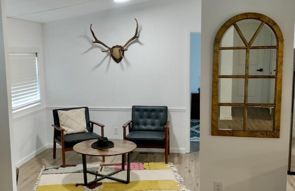 Una habitación con dos sillas, una mesa redonda, un cornamenta montado y un amplio ventanal de arco.