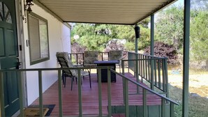A covered porch with a table and chairs, a door, and a view of trees and shrubs. - Cozy Lake House Surrounded by Mountain's (Wofford Heights)