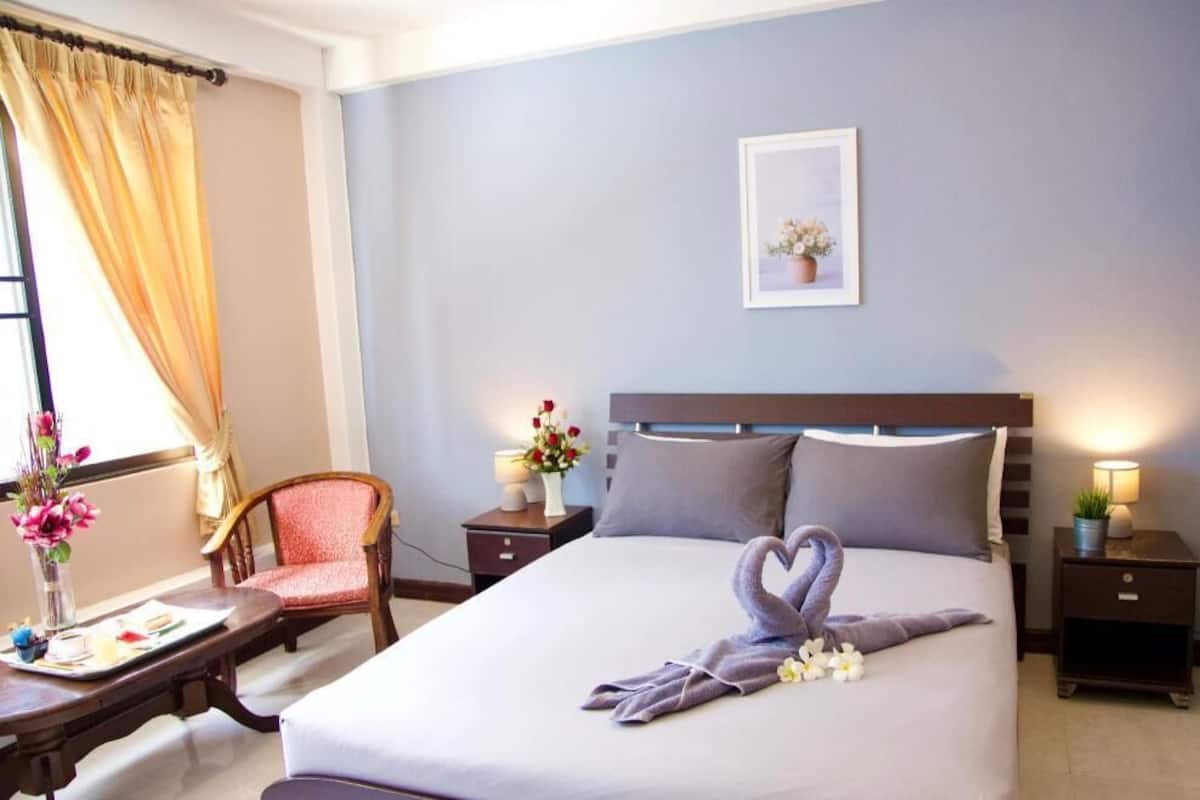 Ein Hotelzimmer mit Bett, Stuhl, Nachttisch, Lampe und einem Fenster mit Vorhängen.