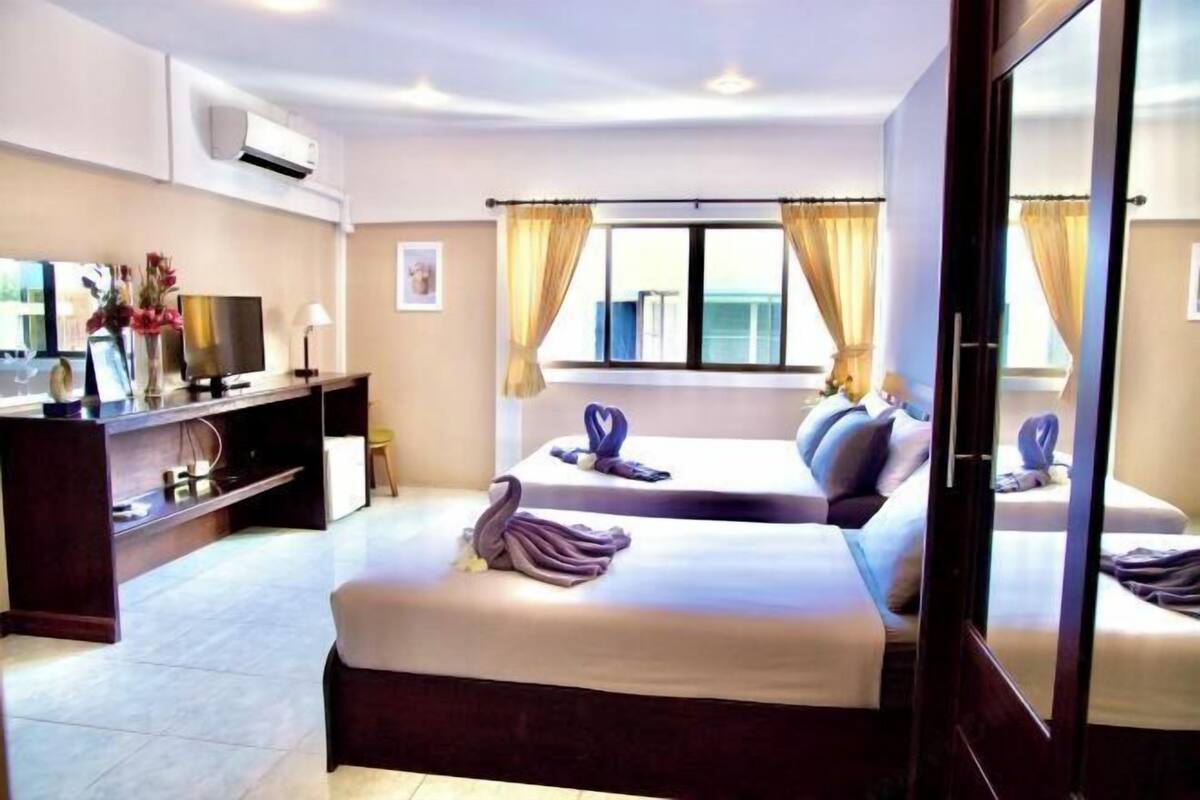 Ein Hotelzimmer mit zwei Betten, einem Fernseher, einem Schreibtisch und einem großen Fenster mit Vorhängen.