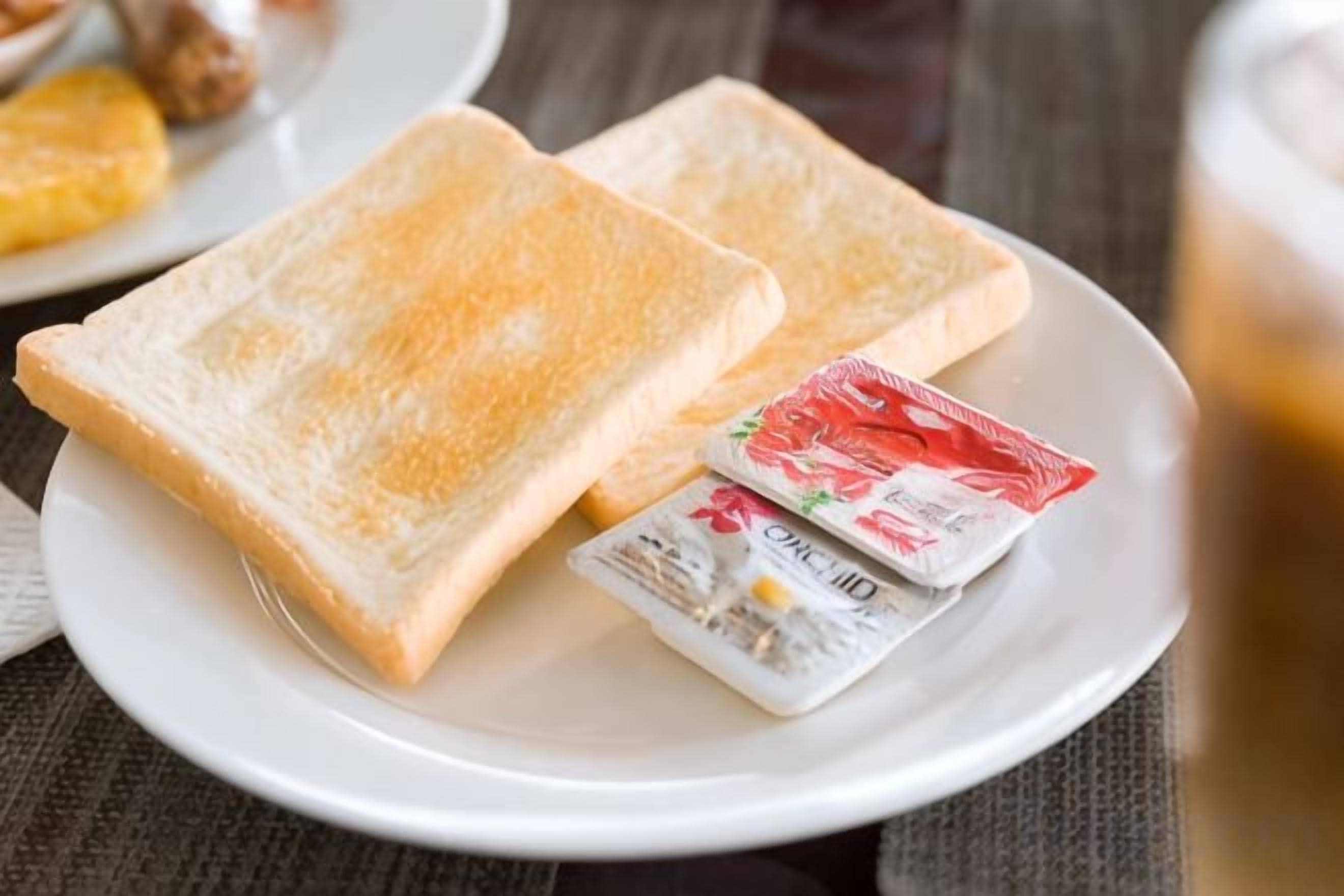 A plate with two slices of toast and two packets of spread on a table.