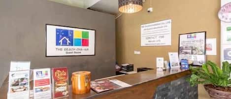 Un mostrador de recepción de hotel con un cartel de bienvenida enmarcado, folletos informativos y una planta en maceta.