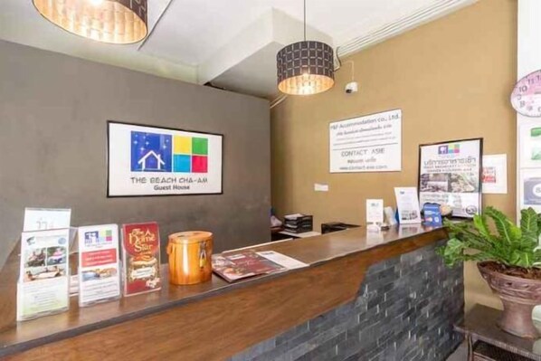 Un mostrador de recepción de hotel con un cartel de bienvenida enmarcado, folletos informativos y una planta en maceta.