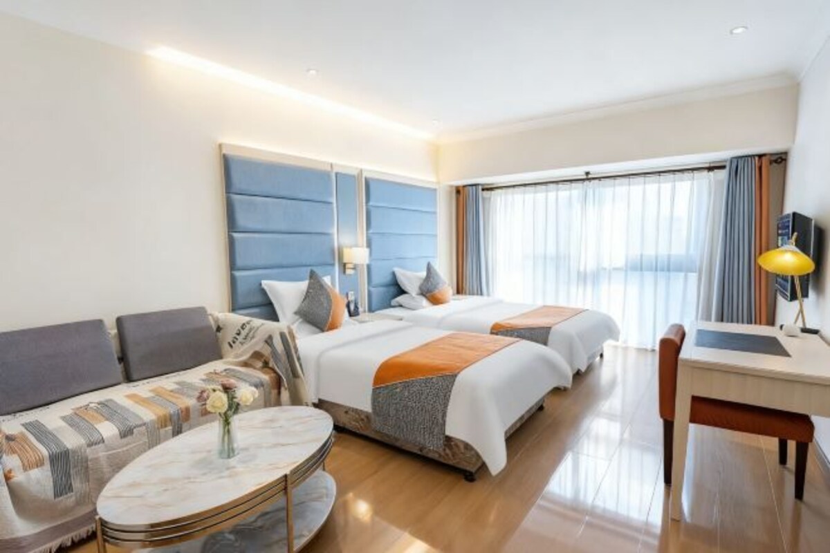 Une chambre d’hôtel avec deux lits, un canapé, un bureau et une grande fenêtre.