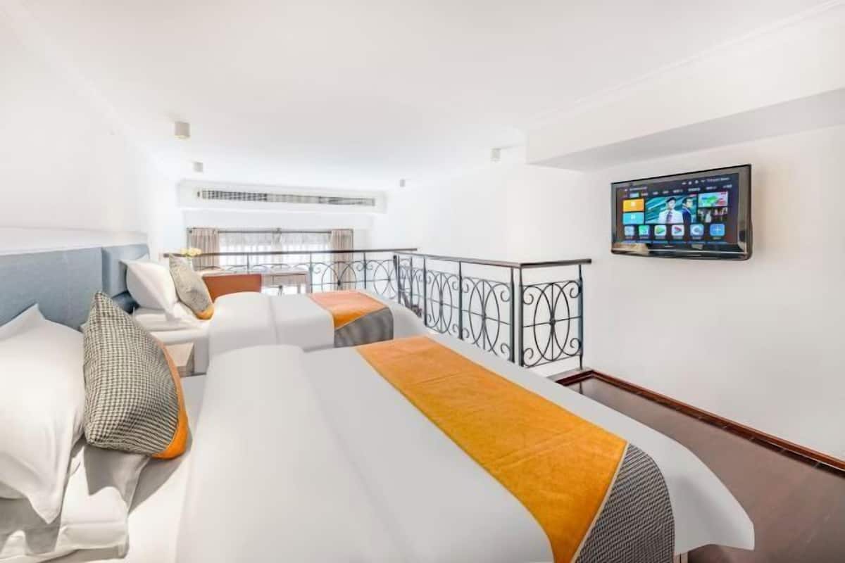 A hotel room with two beds, a balcony, and a mounted TV displaying a hotel app.