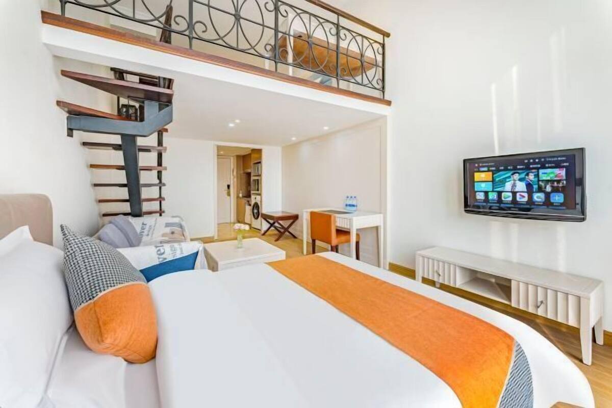 A hotel room with a bed, a desk, a chair, a TV, and a staircase.