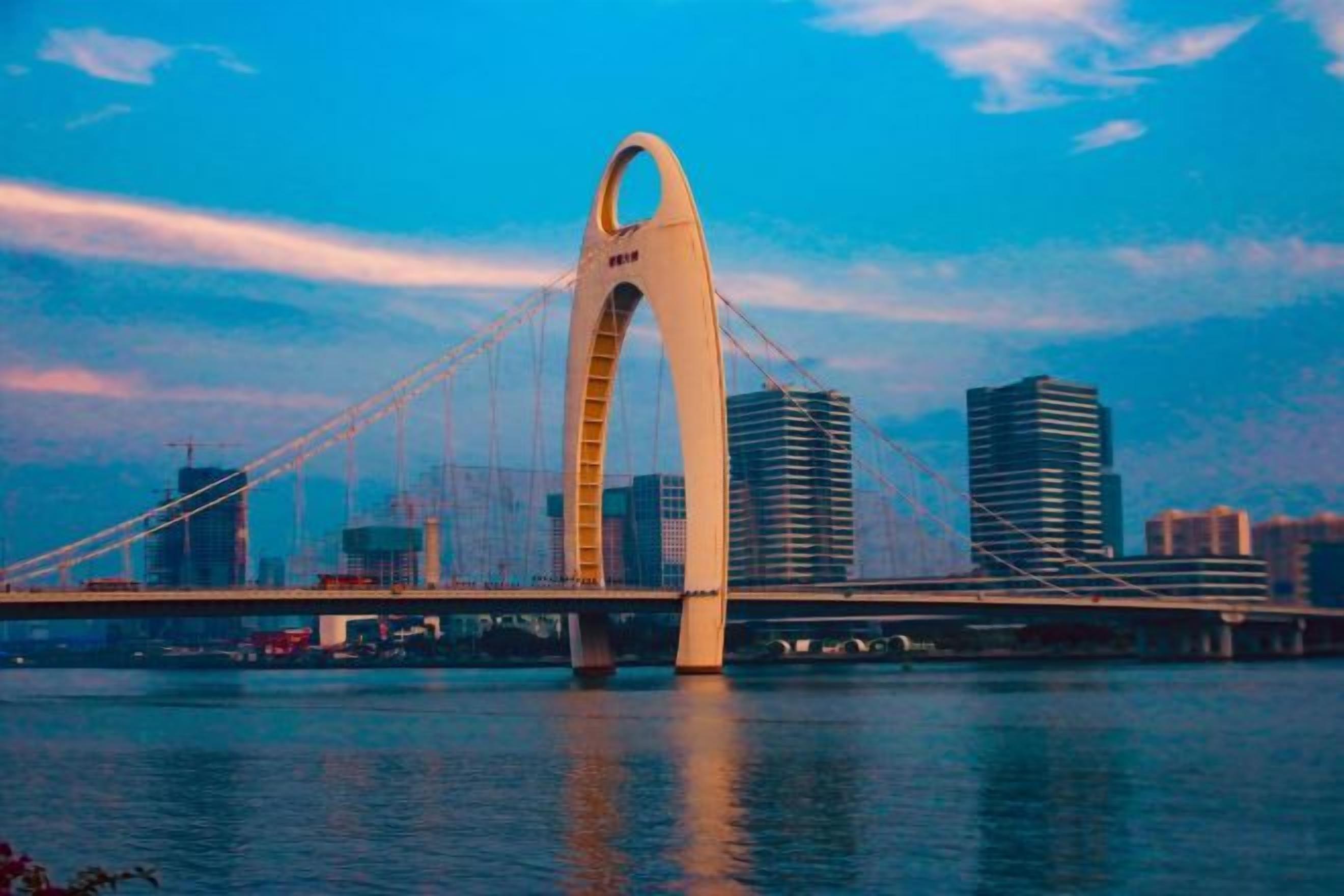 A large bridge with a distinctive arch design, spanning over a body of water with a city skyline in the background.
