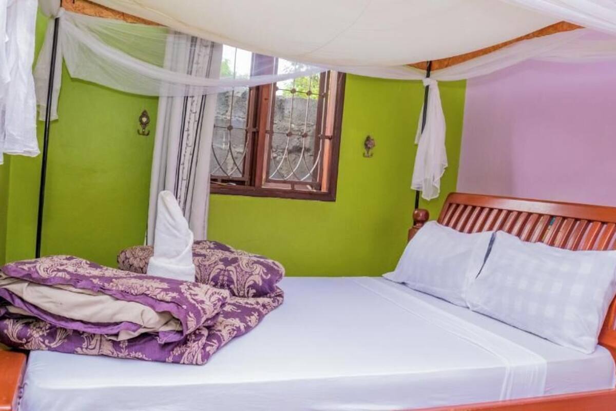 A bed with a canopy, a window with bars, and a green wall.