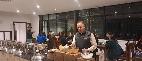 A buffet setup with multiple serving stations, a person preparing food, and guests seated at tables.