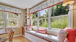 Una habitación con un banco empotrado junto a un ventanal, una silla de madera y una mesa.