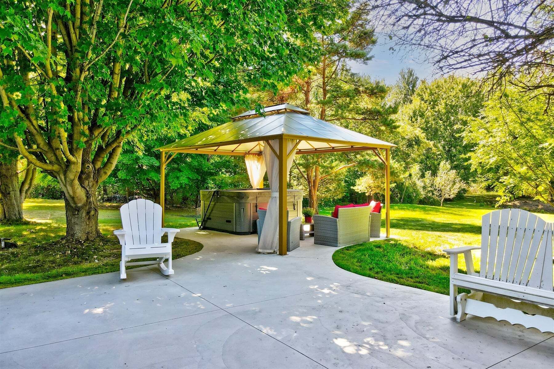A gazebo with a table and chairs, surrounded by trees and grass.