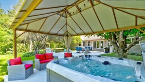Un espacio al aire libre cubierto con un jacuzzi, muebles de mimbre y un patio con sillas y una mesa.
