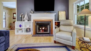 Un salón con chimenea, un televisor montado en la pared y una ventana con vistas a zonas verdes.
