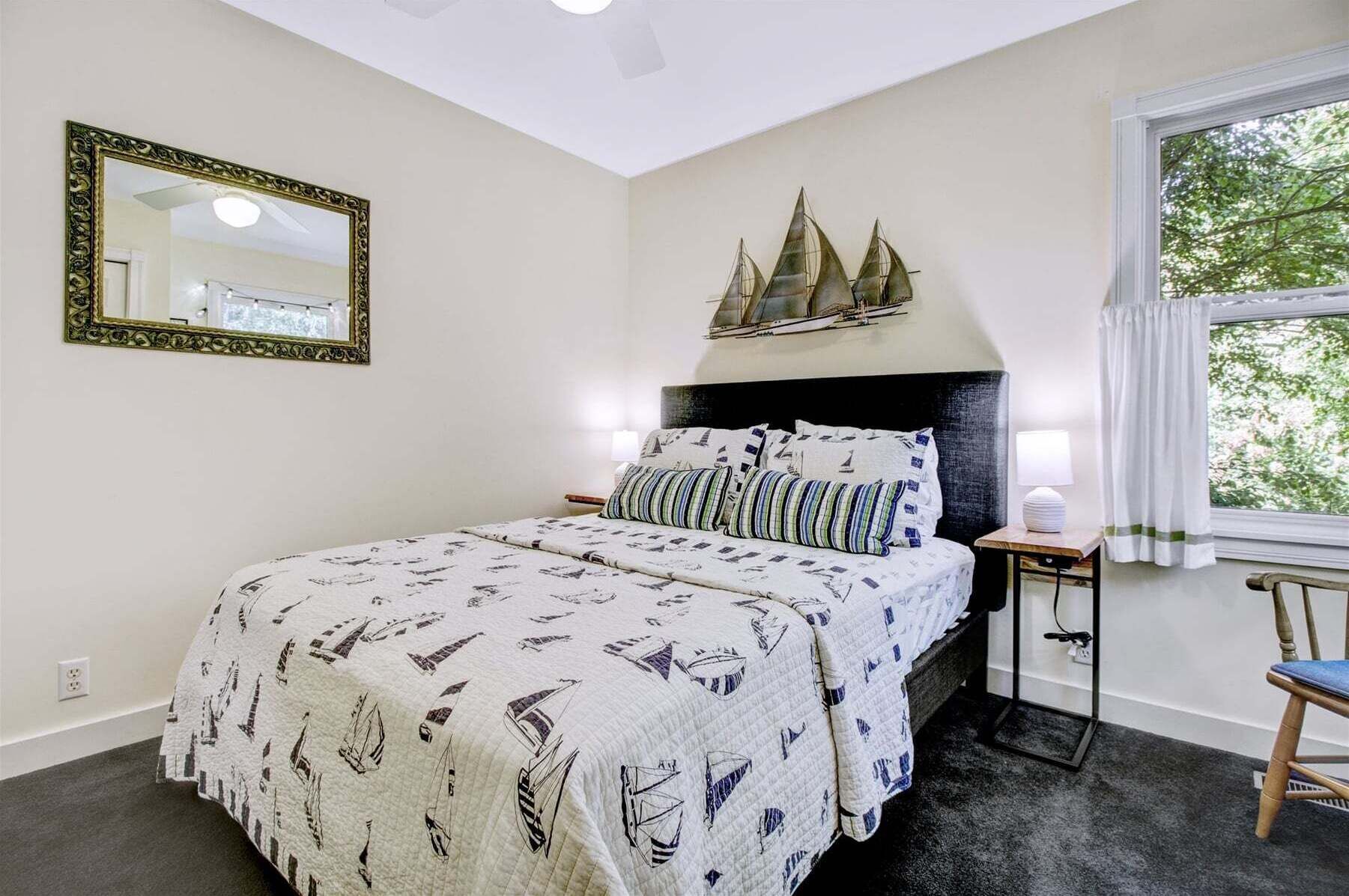 A bedroom with a bed, a nightstand, a lamp, a chair, a window, and a decorative ship model on the wall.