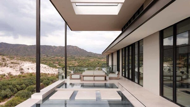 Un área de piscina moderna al aire libre con barandilla de vidrio, asientos y vistas al paisaje desértico.