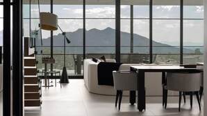 Amplia sala de estar con un ventanal que ofrece vistas a las montañas, un sofá moderno y una mesa de comedor con sillas.