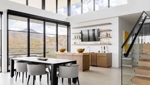 Una cocina moderna con un ventanal grande, una zona de comedor con mesa y sillas, y una escalera de madera.