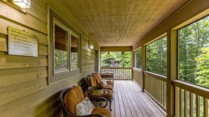 A covered porch with wooden benches and a view of the forest.