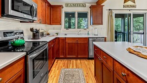 A kitchen with wooden cabinets, stainless steel appliances, a window with a view of greenery, and a star decoration on the ceiling.