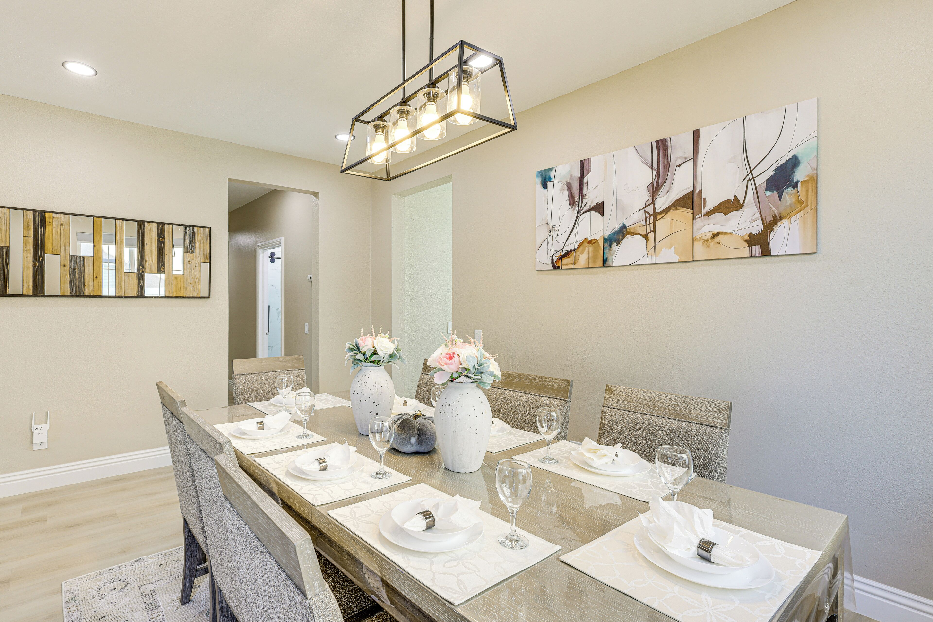 A dining room with a long table set for six, featuring white plates, glasses, and vases with flowers.