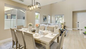 A dining area with a wooden table set for six, surrounded by chairs. There is a chandelier above the table, and the room has large windows allowing natural light. - Mtn-view Gem w/ Private Yard: Luxe Beaumont Home (Beaumont)