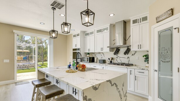 A modern kitchen with white cabinets, a large island with stools, pendant lighting, and a view of the backyard. - Mtn-view Gem w/ Private Yard: Luxe Beaumont Home (Beaumont)