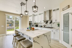 Une cuisine moderne avec des armoires blanches, un grand îlot central doté de tabourets, un éclairage suspendu et une vue sur le jardin.