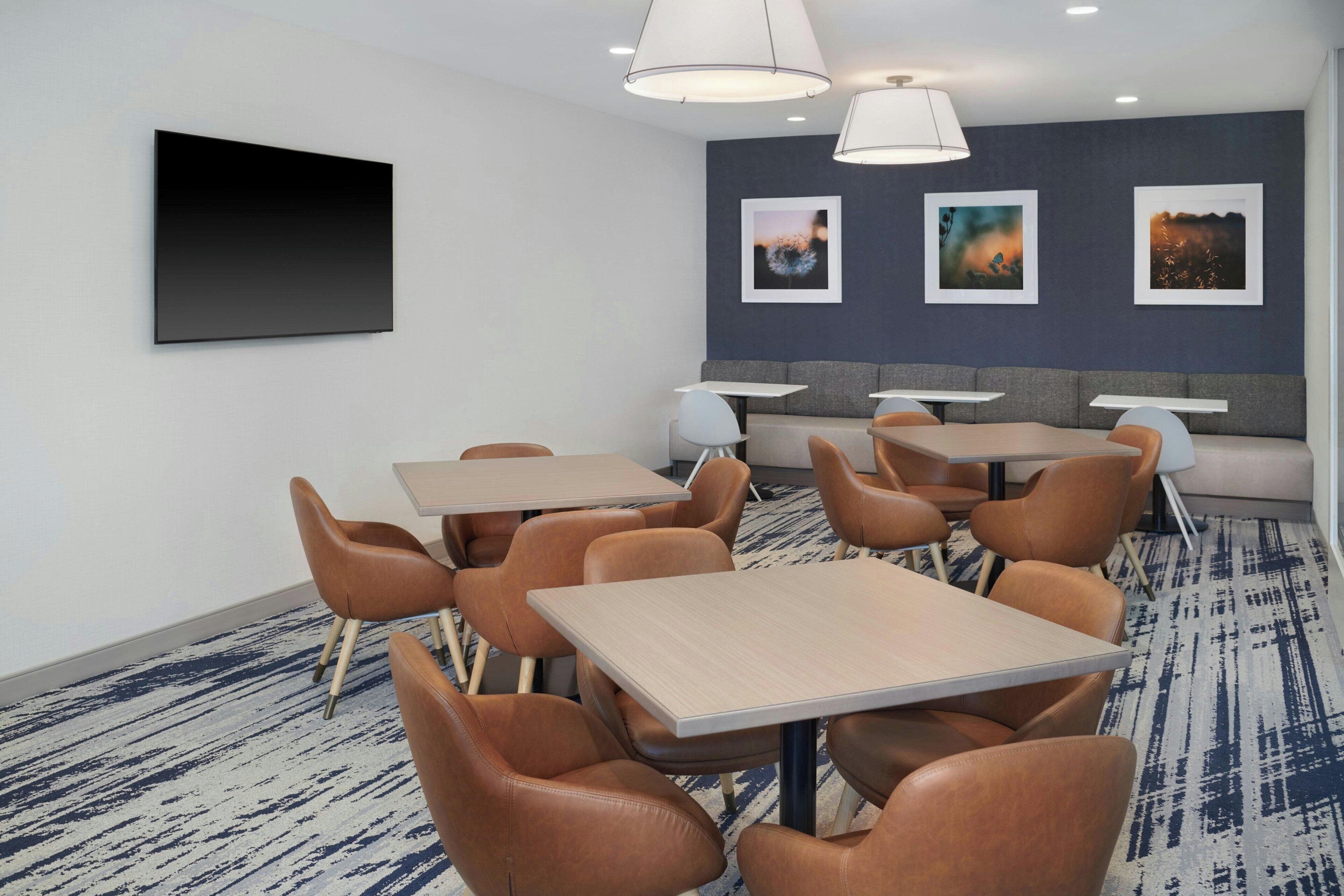Et moderne hotelværelse med et stort fladskærms-tv, flere siddepladser og billedkunst på væggene.