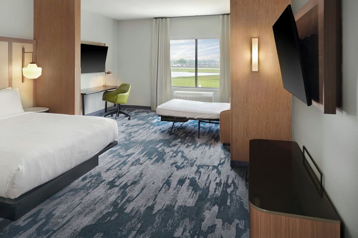 A hotel room with a large bed, a desk, a chair, a TV, and a view of the outdoors.