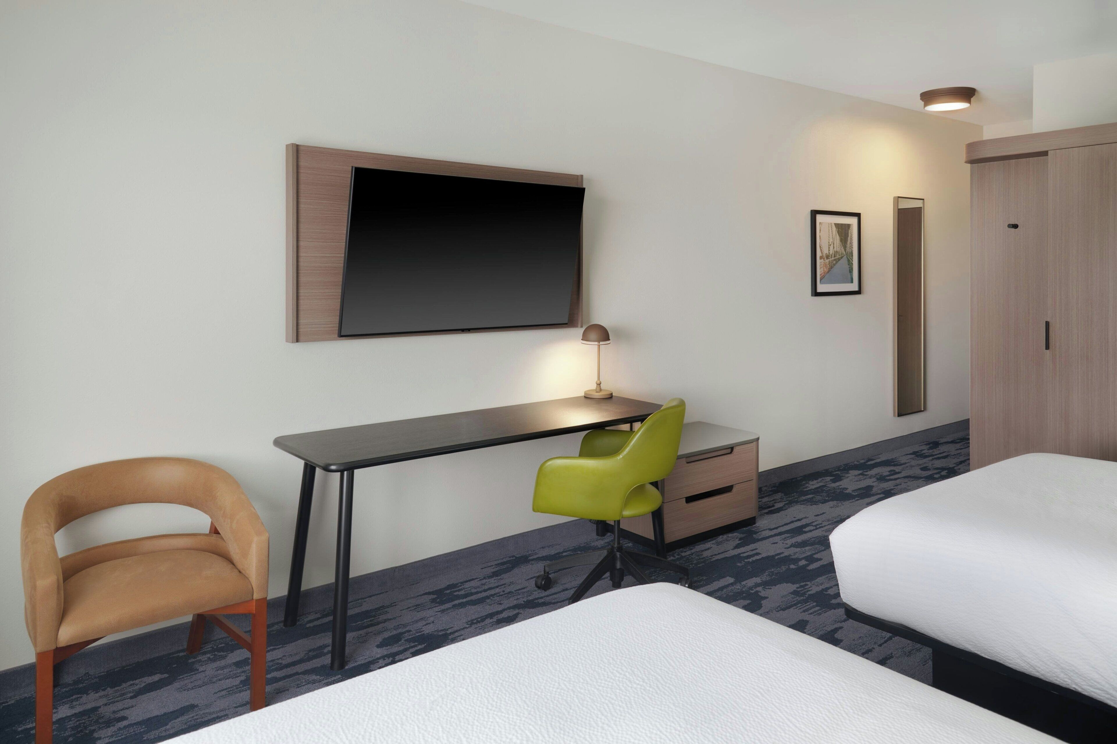 A hotel room with a bed, a desk with a chair, a TV mounted on the wall, and a wardrobe.