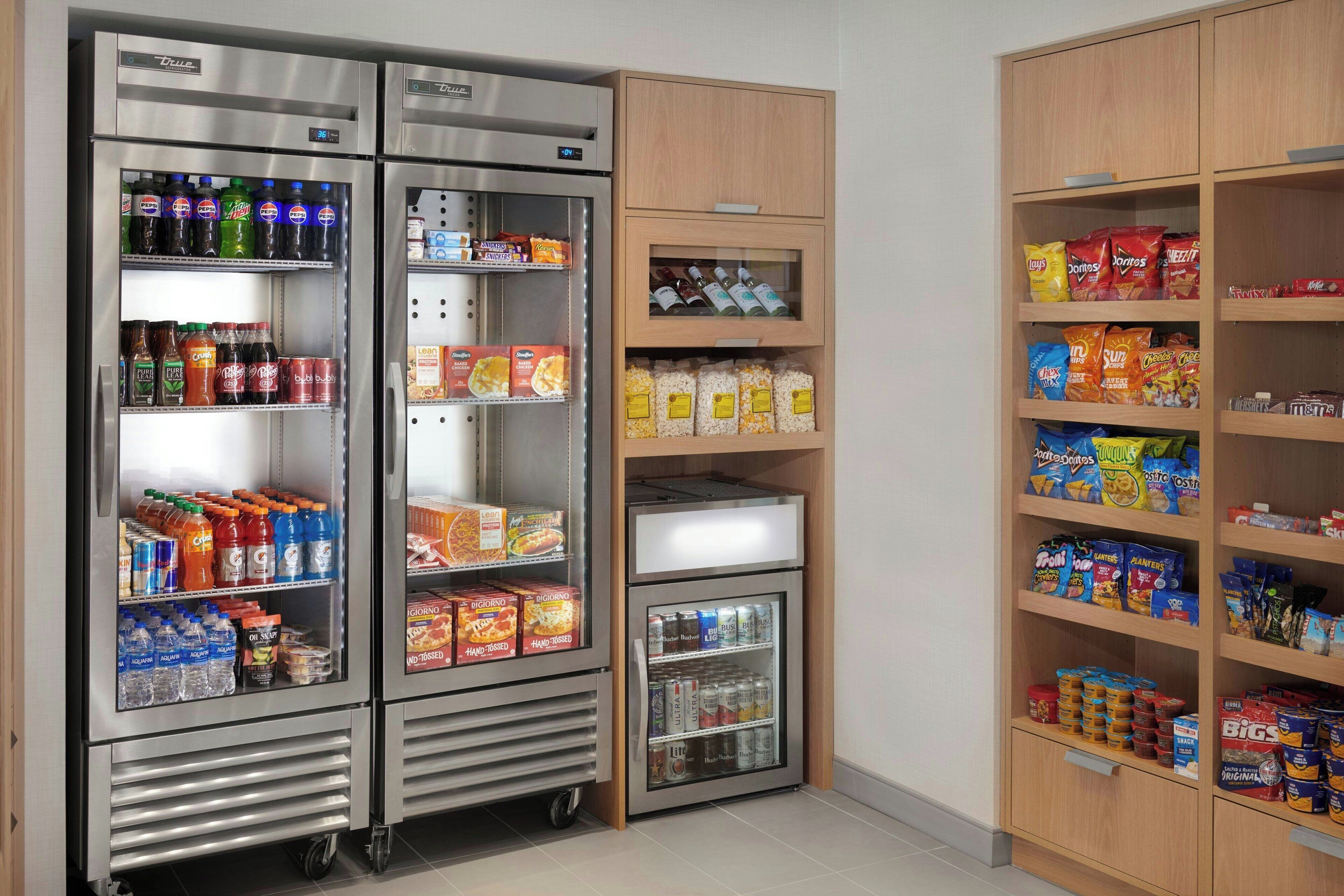 A mini-fridge stocked with beverages and snacks, a small refrigerator with drinks, and shelves with various food items.