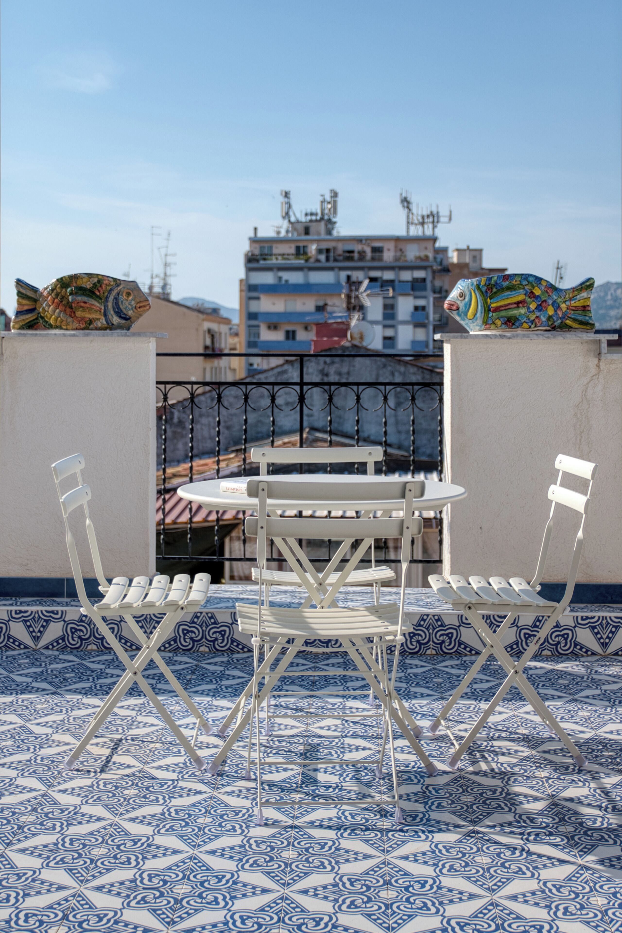 A terrace with a table and chairs, patterned floor tiles, and a view of buildings in the background.